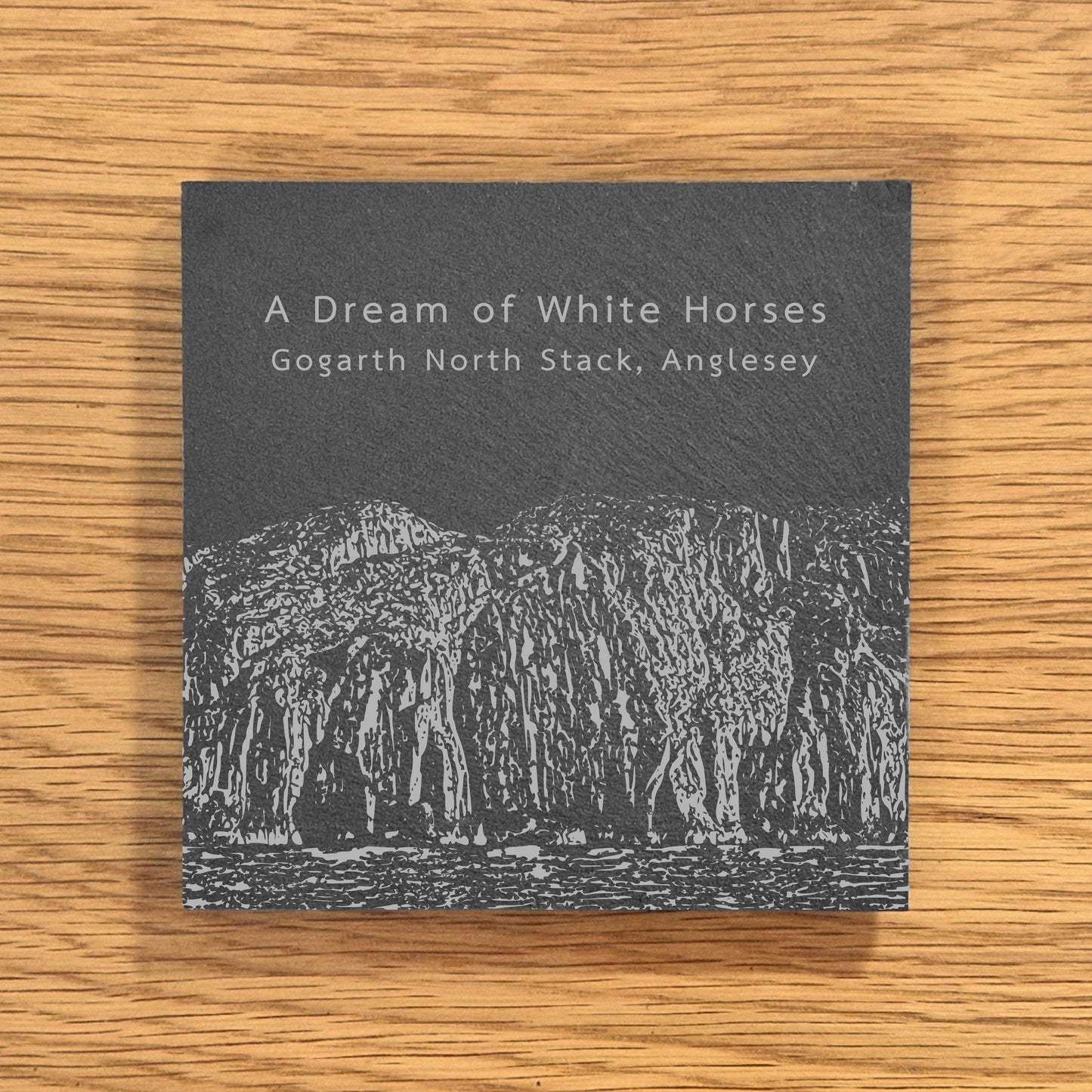 Slate coaster engraved with image of Gogarth North Stack, a popular climbing location, displayed on a wooden surface.