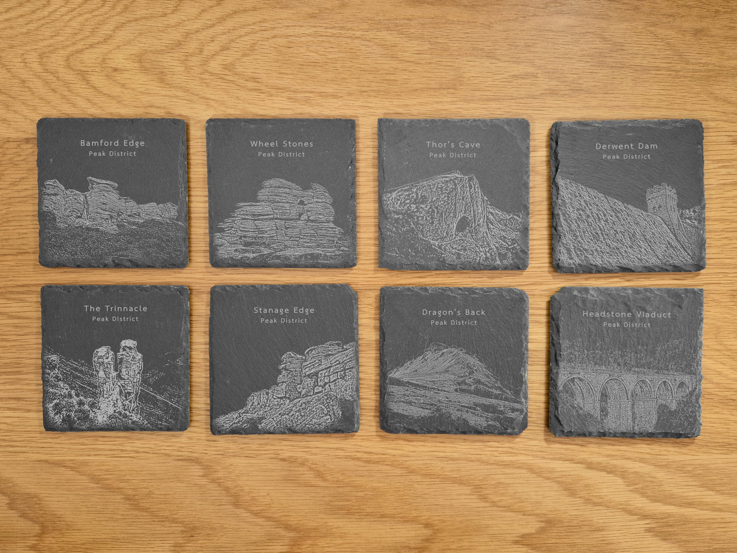 Set of 8 slate coasters engraved with Peak District landmarks on a wooden surface