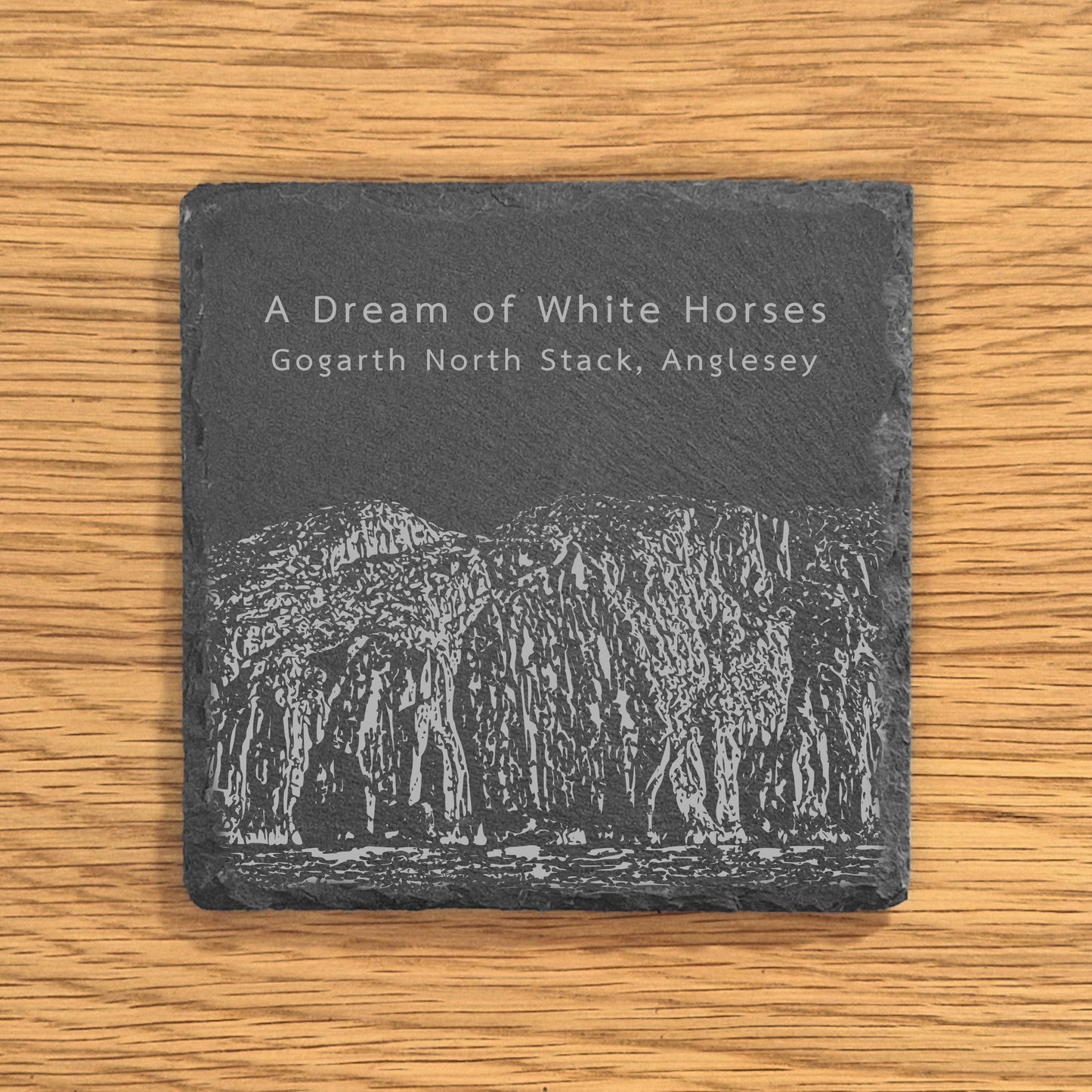 Slate coaster engraved with image of Gogarth North Stack, a popular climbing location, displayed on a wooden surface.