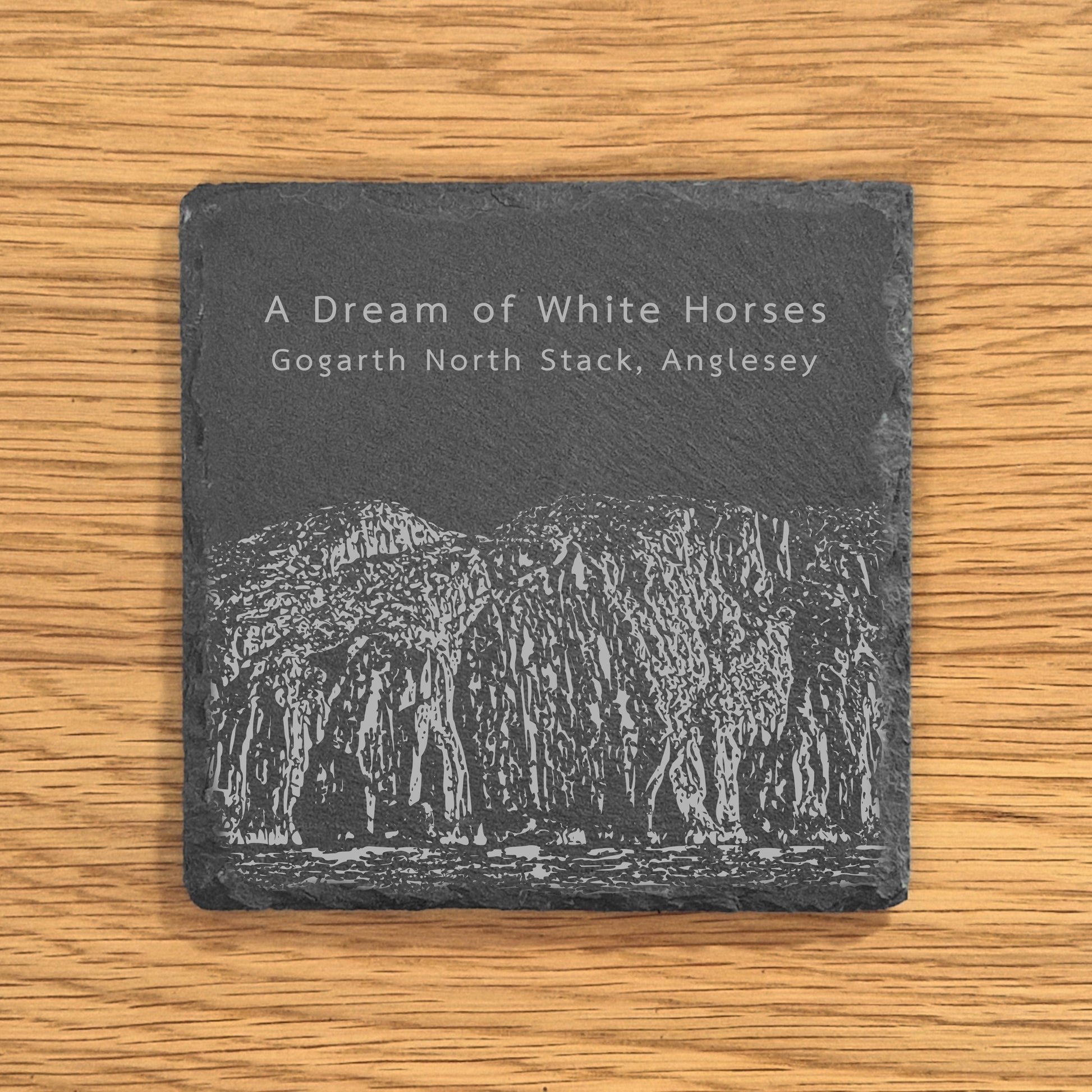 Slate coaster engraved with image of Gogarth North Stack, a popular climbing location, displayed on a wooden surface.