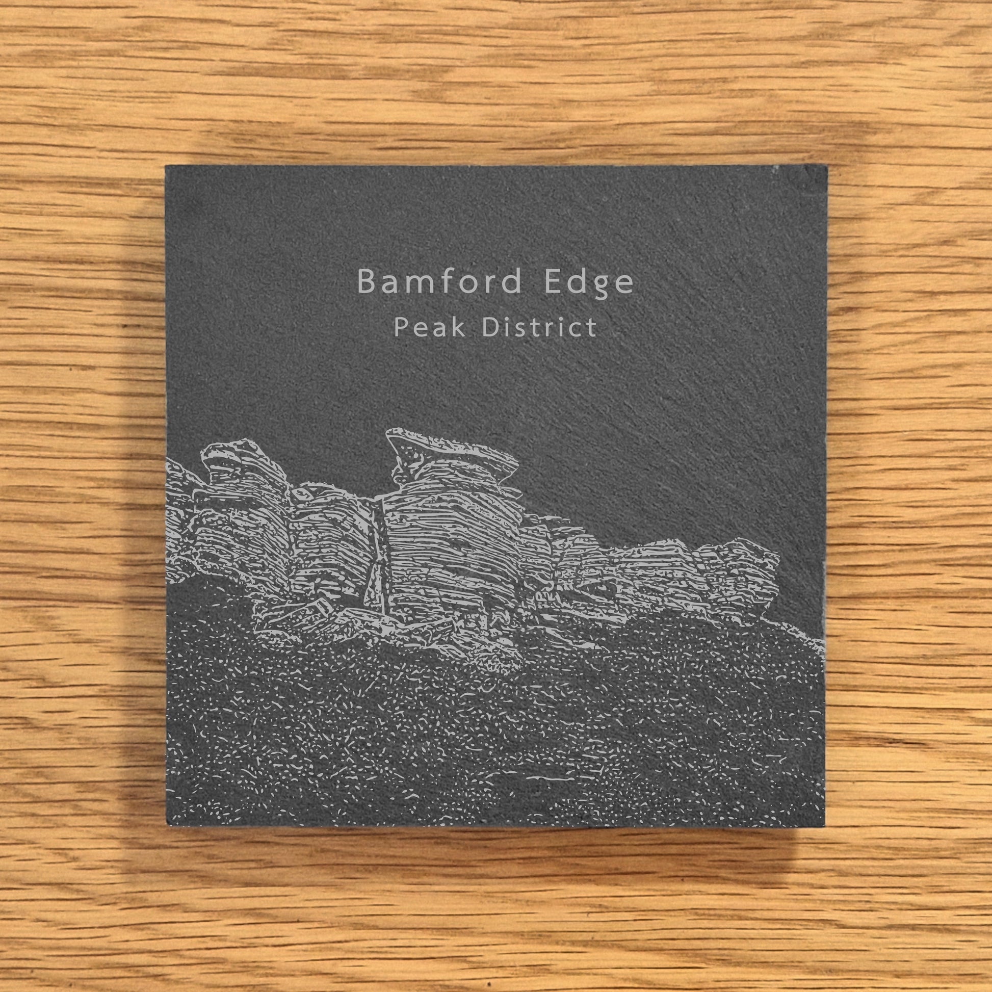 Slate coaster with engraved image of Bamford Edge in the Peak District on a wooden surface