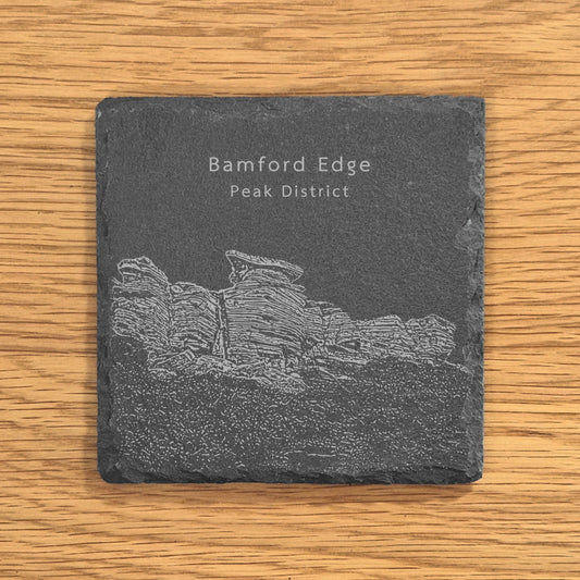 Slate coaster with engraved image of Bamford Edge in the Peak District on a wooden surface.