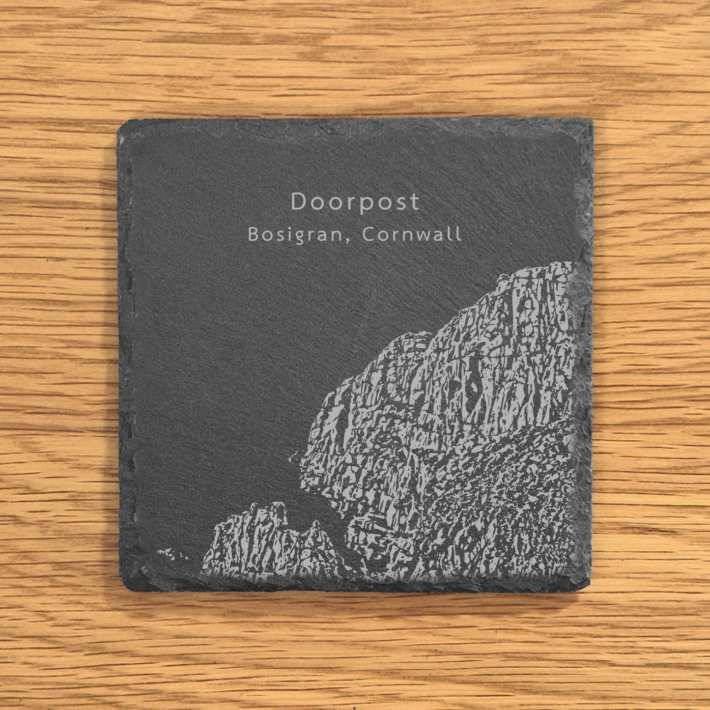 Slate coaster engraved with image of a popular climbing location, Doorpost (Bosigran, Cornwall), displayed on a wooden surface.