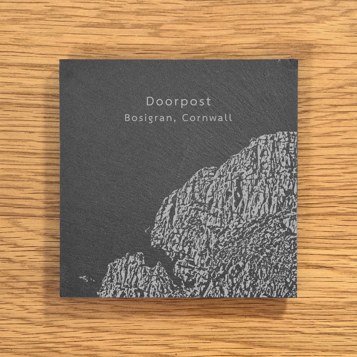 Slate coaster engraved with image of a popular climbing location, Doorpost (Bosigran, Cornwall), displayed on a wooden surface.