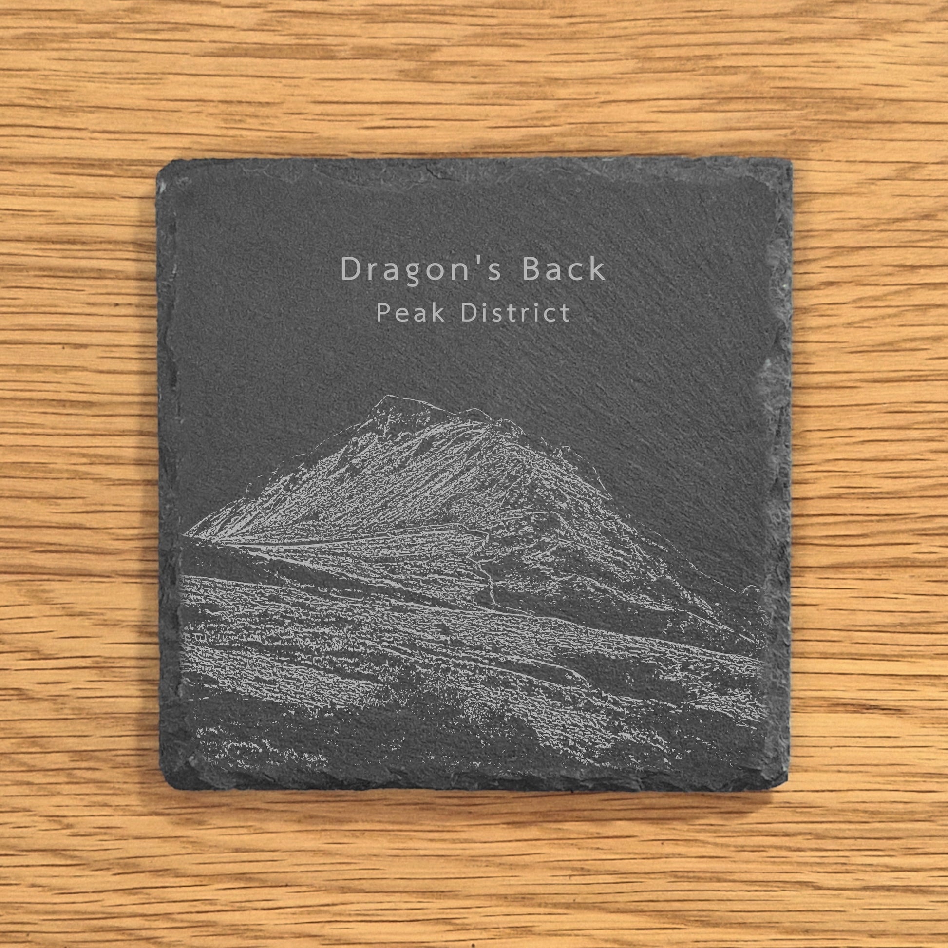 Slate coaster with engraved image of the Dragon's Back (Chrome Hill) in the Peak District on a wooden surface.