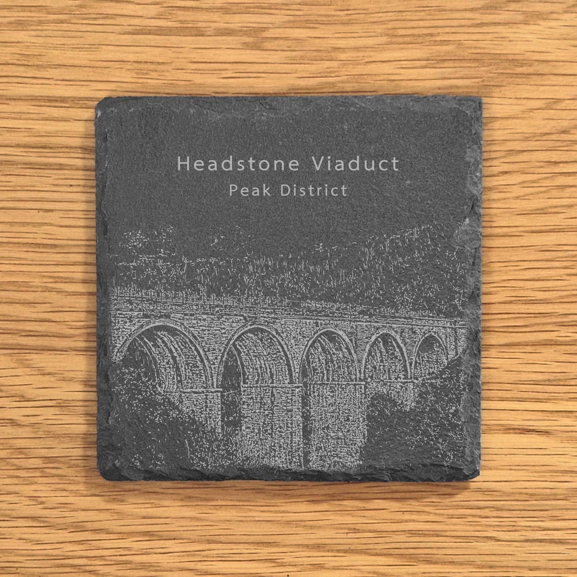 Slate coaster with engraved image of Headstone Viaduct in the Peak District on a wooden surface.