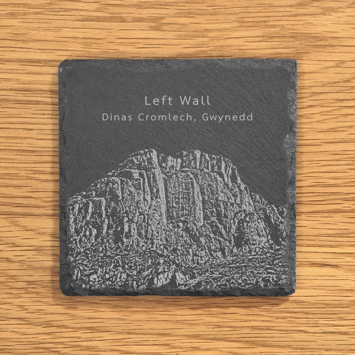 Slate coaster with engraved image of a popular climbing location Left Wall in Dinas Cromlech, Gwynedd on a wooden surface.