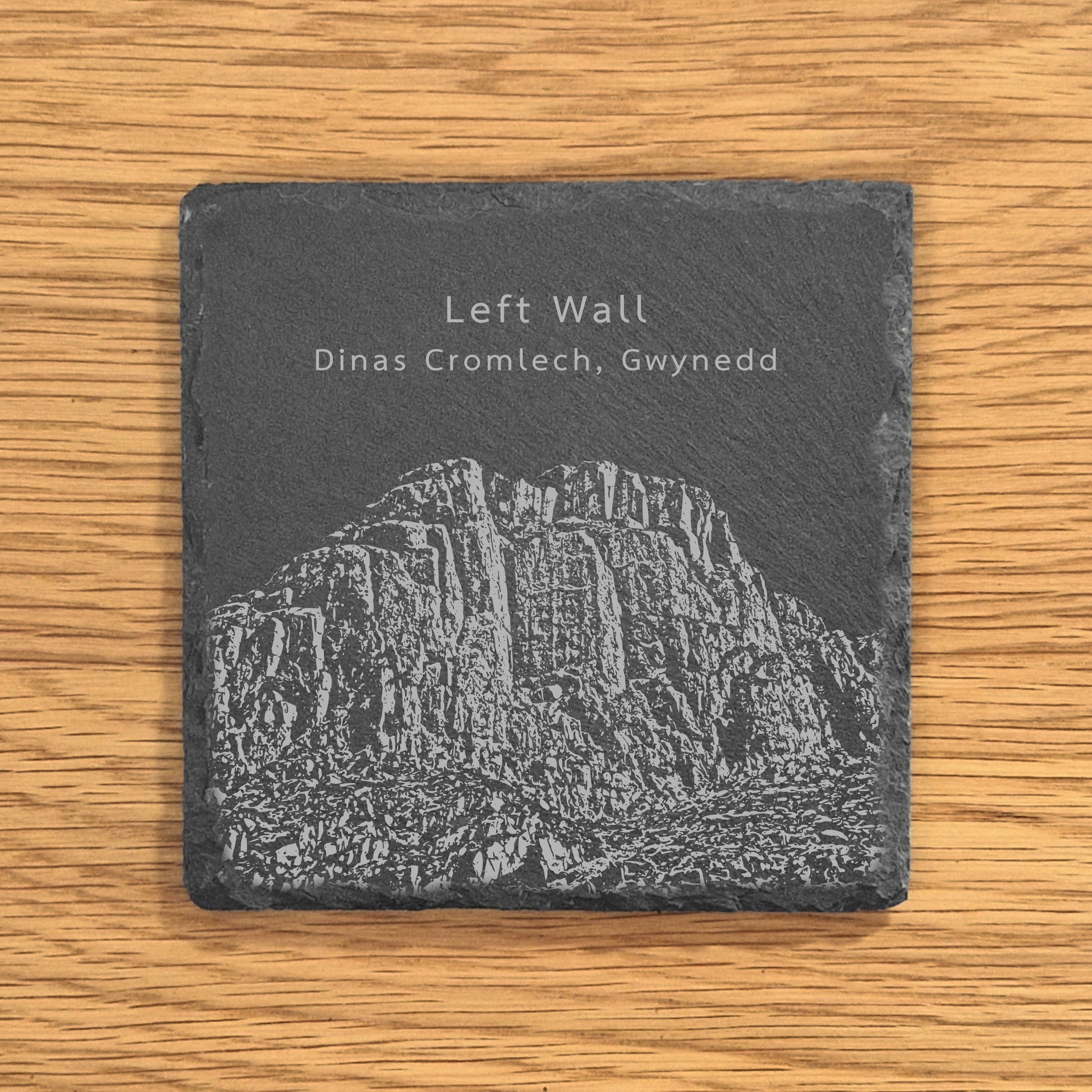 Slate coaster with engraved image of a popular climbing location Left Wall in Dinas Cromlech, Gwynedd on a wooden surface.