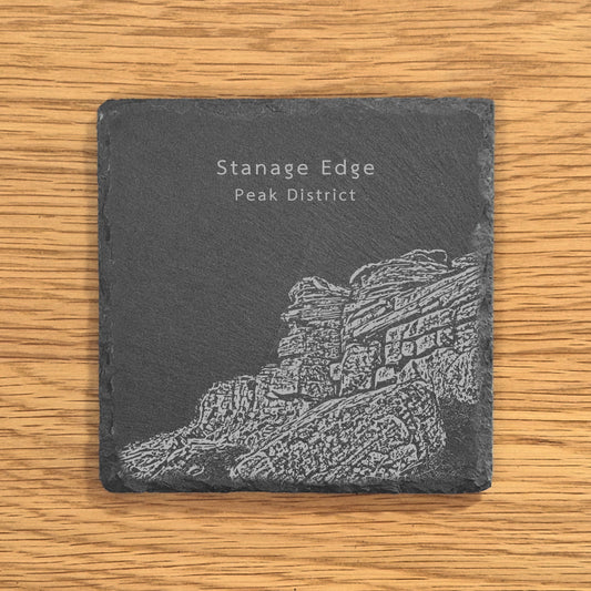 Slate coaster with engraved image of Stanage Edge in the Peak District on a wooden surface.