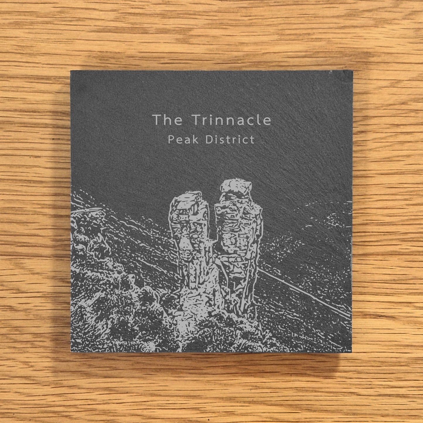 Slate coaster with engraved image of The Trinnacle in the Peak District on a wooden surface.