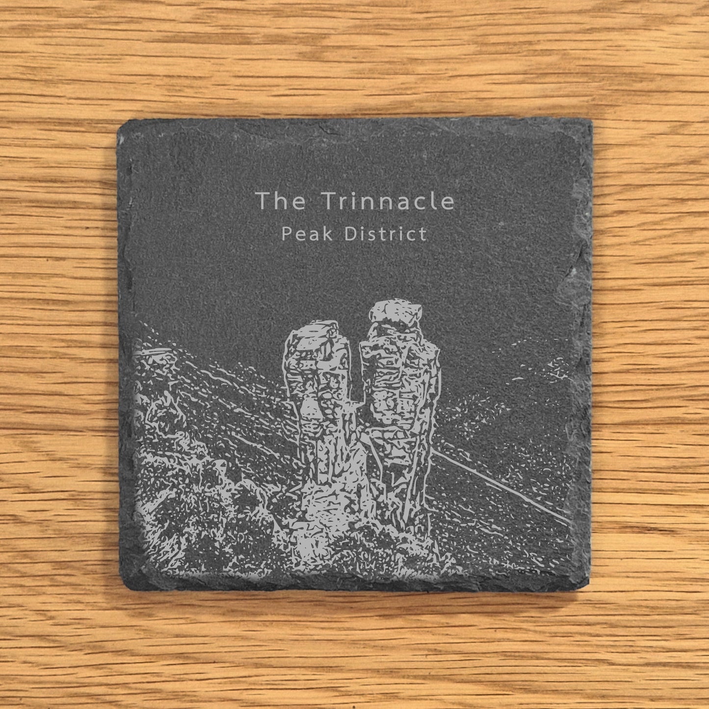 Slate coaster with engraved design of The Trinnacle in the Peak District on a wooden surface.