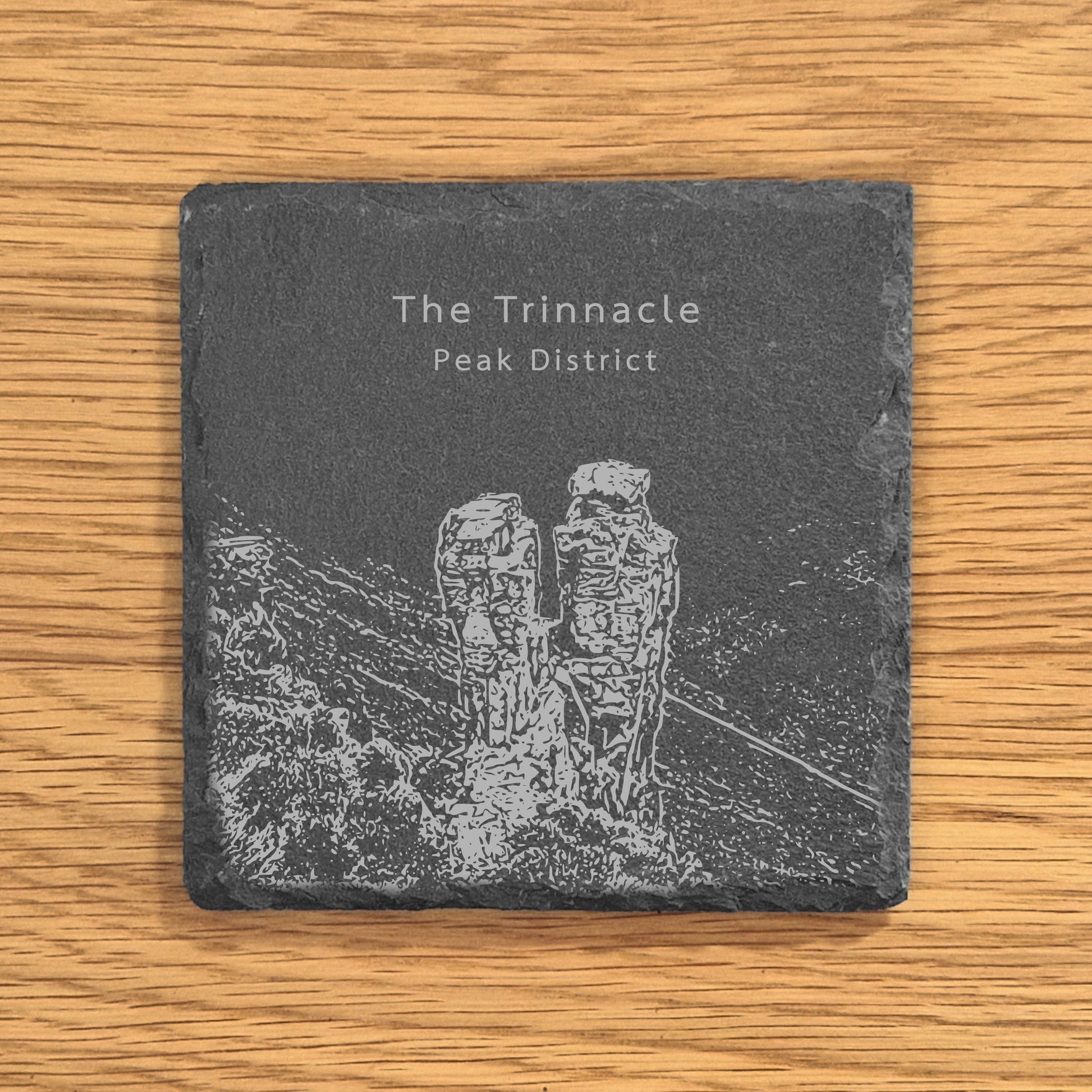 Slate coaster with engraved design of The Trinnacle in the Peak District on a wooden surface.