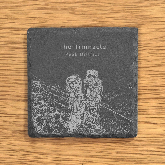 Slate coaster with engraved design of The Trinnacle in the Peak District on a wooden surface.
