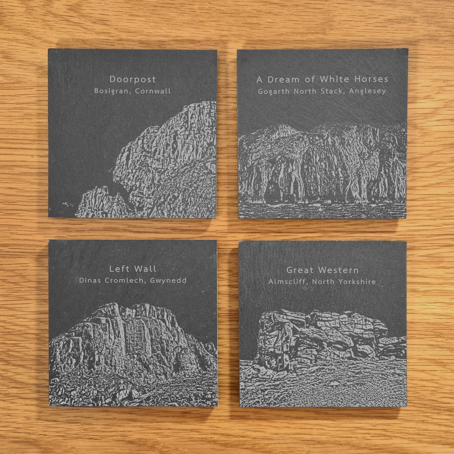 A set of four slate coasters, each engraved with a different popular climbing location: Doorpost, A Dream Of White Horses, Left Wall, and Great Western, displayed on a wooden surface.