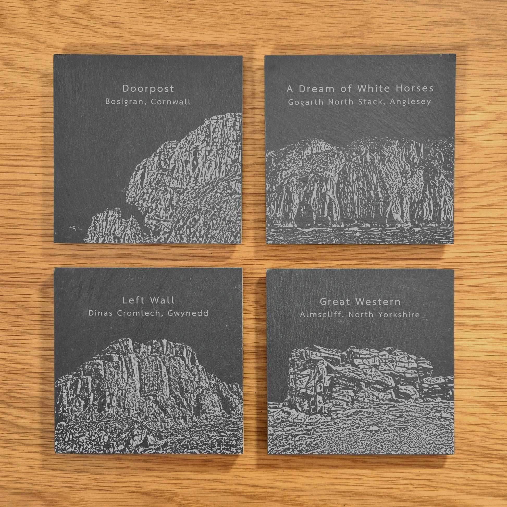 A set of four slate coasters, each engraved with a different popular climbing location: Doorpost, A Dream Of White Horses, Left Wall, and Great Western, displayed on a wooden surface.