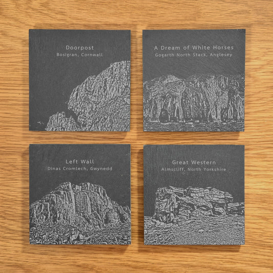 A set of four slate coasters, each engraved with a different popular climbing location: Doorpost, A Dream Of White Horses, Left Wall, and Great Western, displayed on a wooden surface.