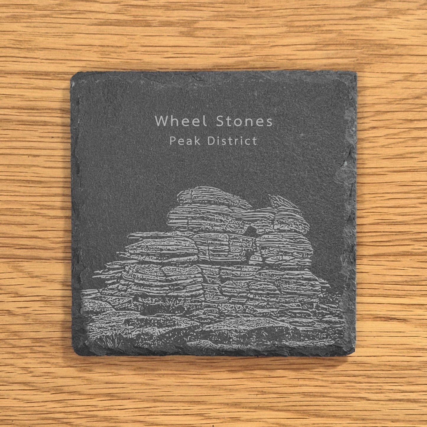 Slate coaster with engraved image of Wheel Stones in the Peak District on a wooden surface.
