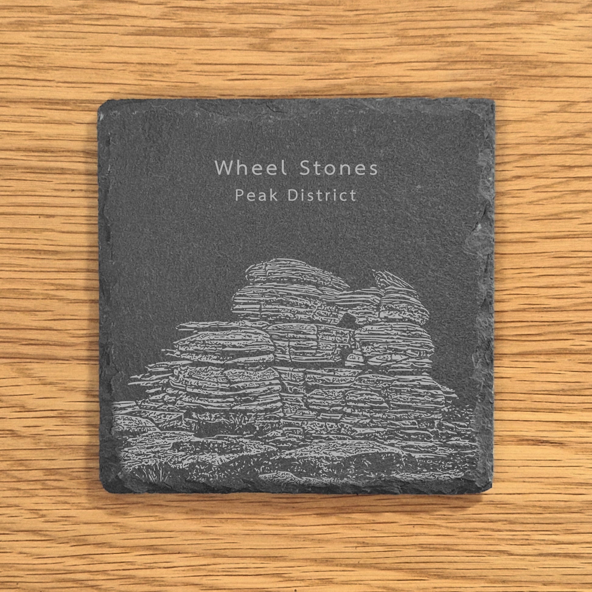 Slate coaster with engraved image of Wheel Stones in the Peak District on a wooden surface.
