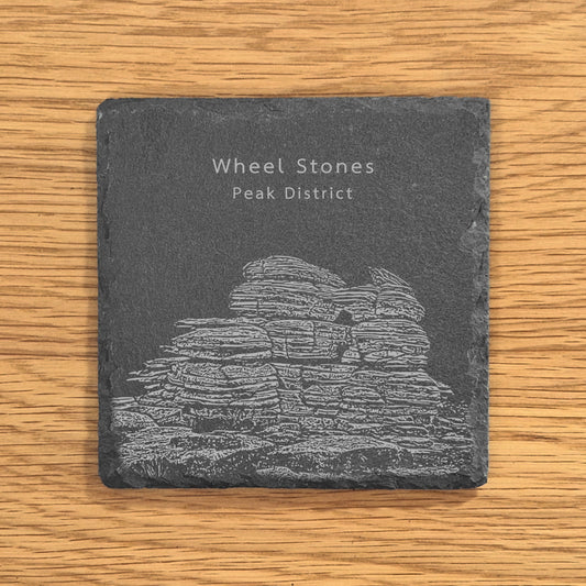 Slate coaster with engraved image of Wheel Stones in the Peak District on a wooden surface.