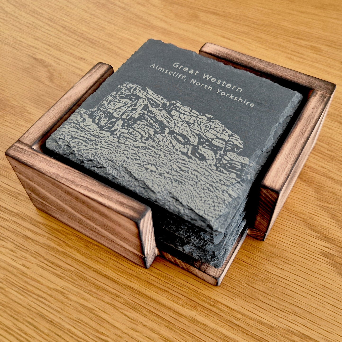 Set of slate coasters in a scorched Beech coaster holder on a wooden surface.